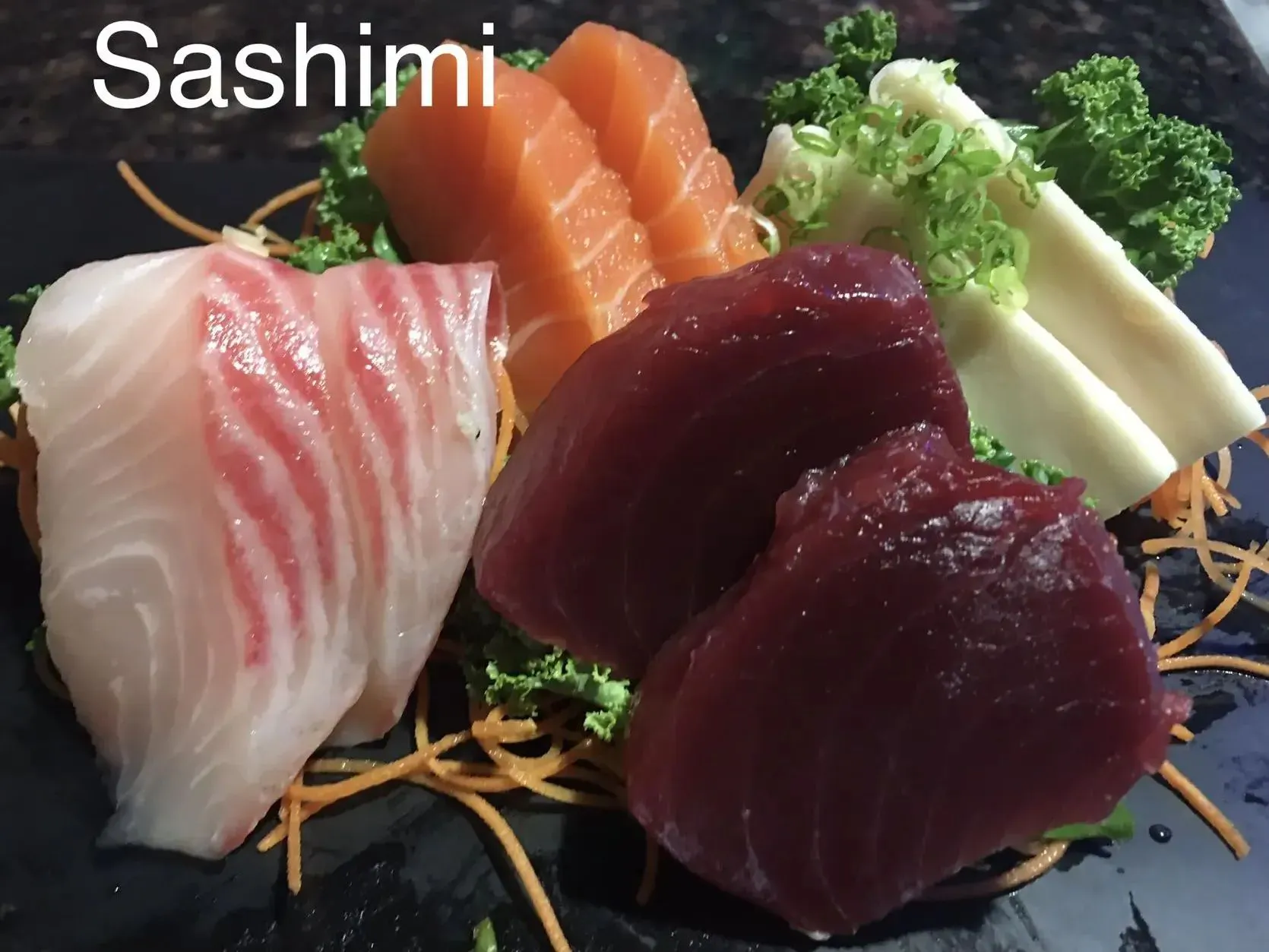 Colorful assorted sashimi platter with salmon, tuna and white fish on dark stone plate